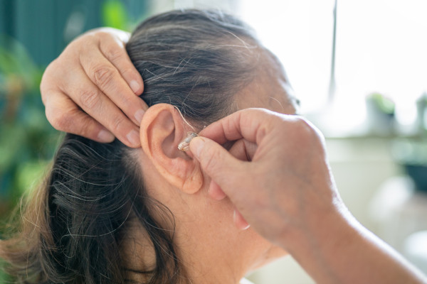 An older woman placing her hearing aid in her ear